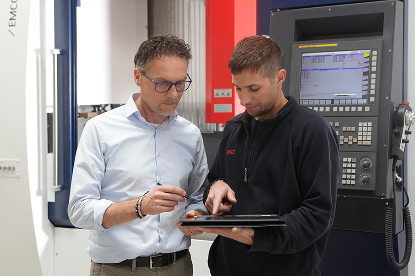 zwei Mitarbeiter besprechen Daten am Tablet vor der EMCO-Maschine
