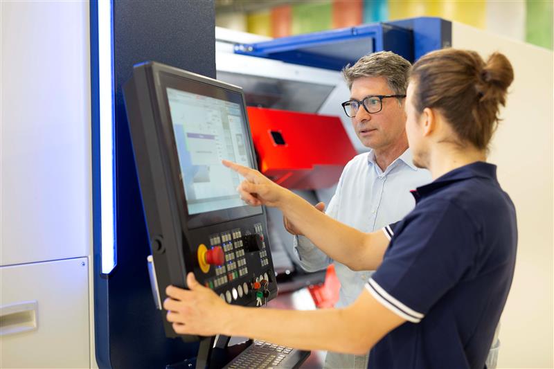 zwei EMCO Mitarbeiter arbeiten an CNC Maschine und sprechen miteinander